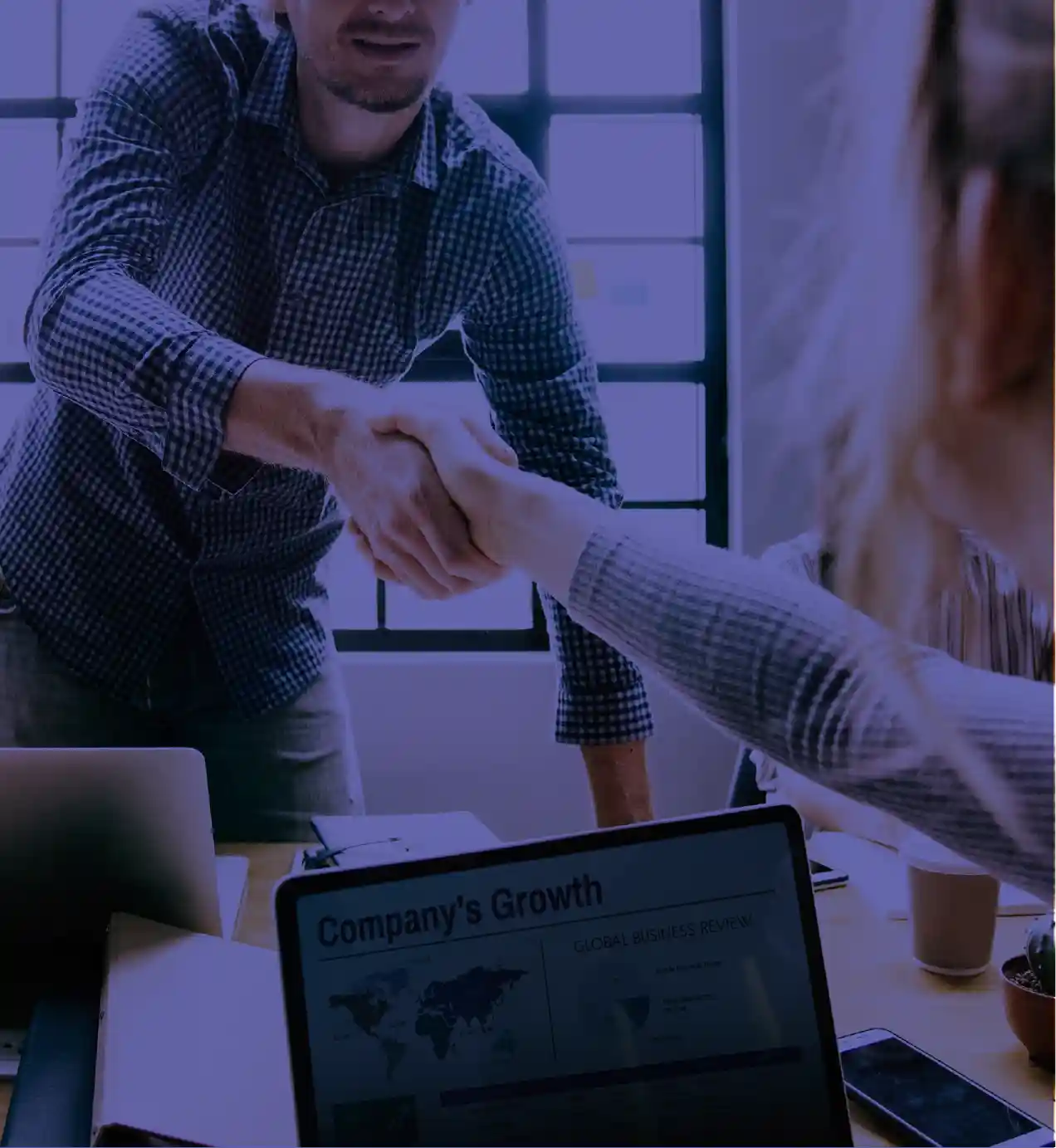 Business professionals shaking hands during a meeting, with a laptop showing company growth data in the foreground.